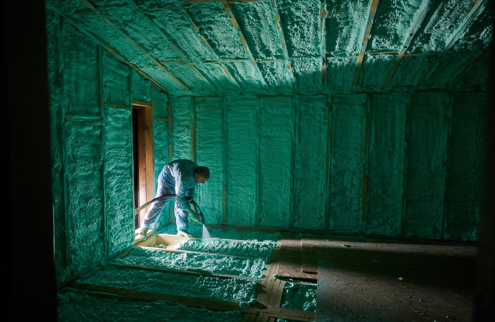 Male builder insulating wooden frame house. Man worker spraying polyurethane foam inside of future cottage, using plural component gun. Construction and insulation concept.